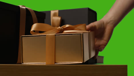 Close-Up-Of-Man-Putting-Down-Gift-Wrapped-Present-In-Box-Decorated-With-Ribbon-On-Table-Shot-Against-Green-Screen